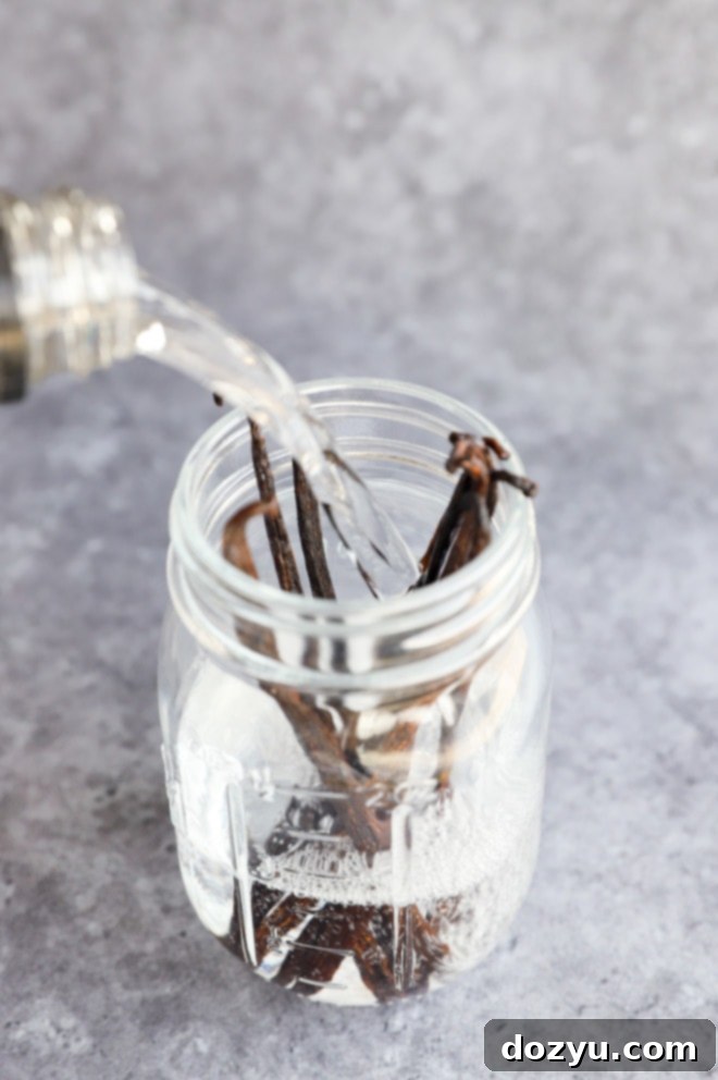 Craft Your Own Vanilla Extract 6 A hand pouring vodka into a mason jar already containing prepared vanilla beans