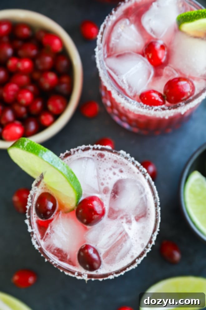 Refreshing Cranberry Margarita 2 Two Cranberry margaritas in elegant cocktail glasses, garnished with fresh cranberries and lime slices, set against a festive, blurred background.