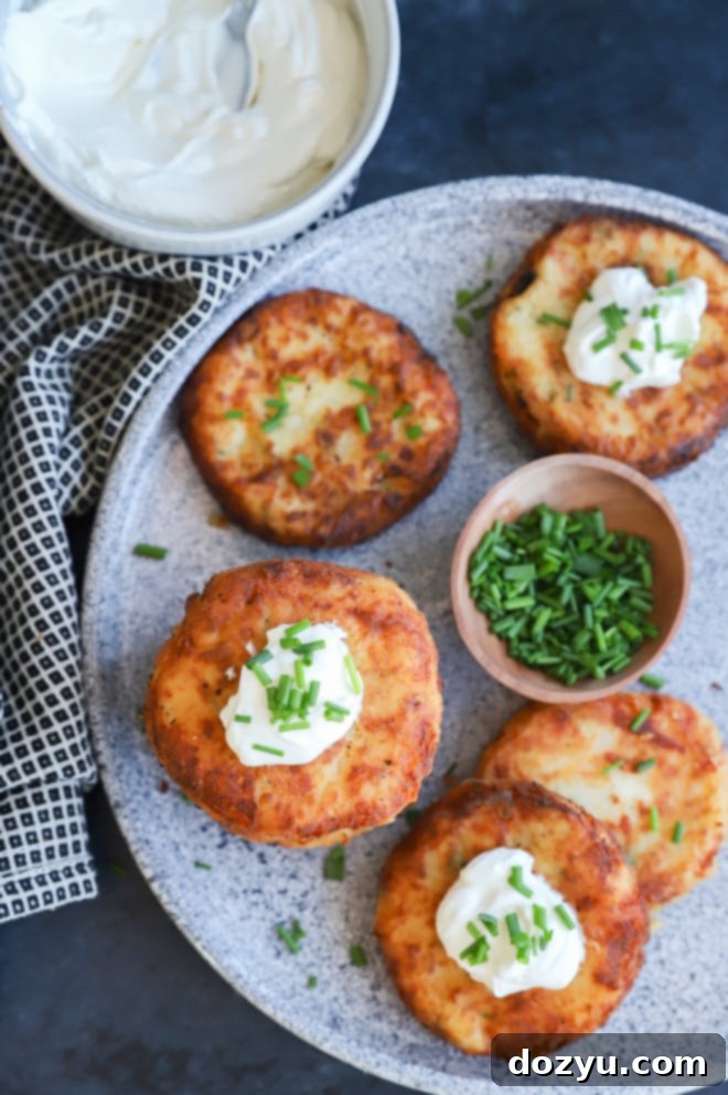Crispy Potato Patties 3 mashed potato pancakes with fresh chives and sour cream on grey platter with linen