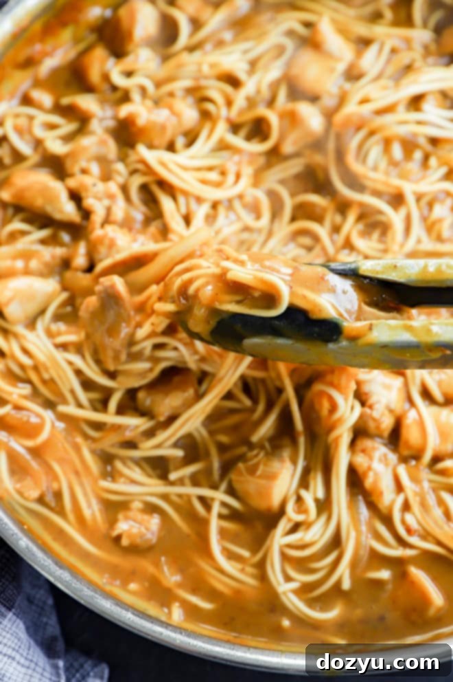 Rich Japanese Curry Udon 5 Kitchen tongs lifting a portion of curry udon noodles and chicken from a large skillet, ready to serve.