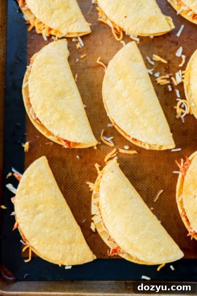 Zesty Crispy Chicken Tacos with Creamy Avocado Tomatillo 7 A baking sheet filled with neatly folded crispy chicken tacos, brushed with oil and ready for the oven.