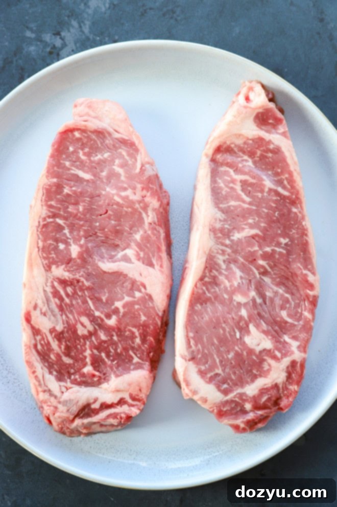 Grilled New York Strip Perfection 4 Raw New York strip steaks on a plate, ready for preparation