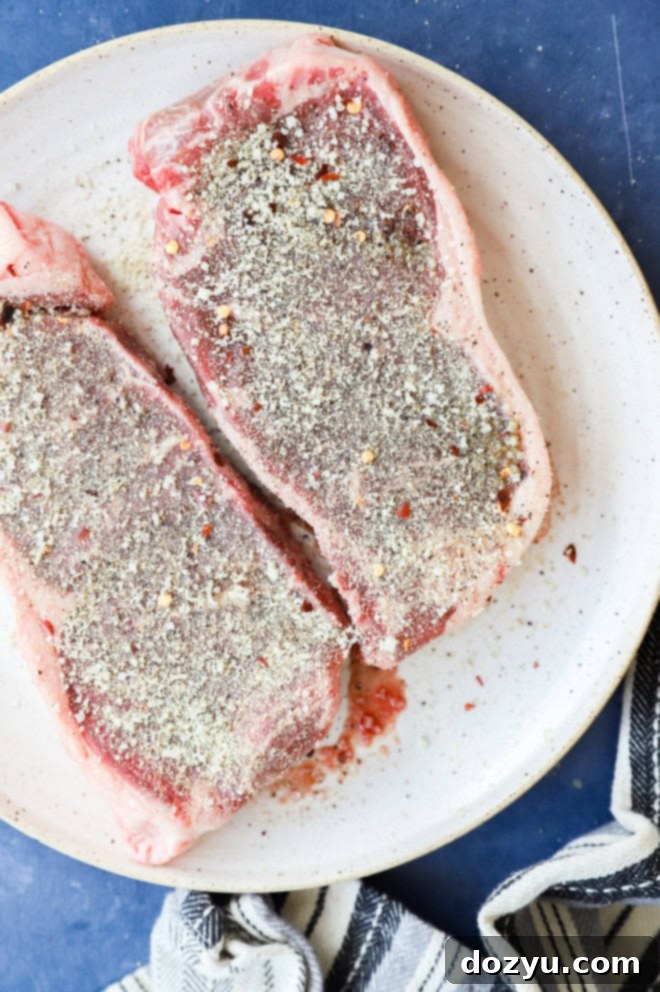 Grilled New York Strip Perfection 6 Raw New York strip steak generously rubbed with steak seasoning on a plate, ready for the grill