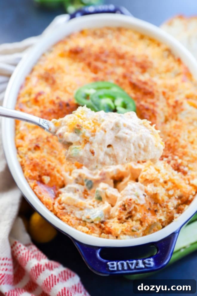 Zingy Cheesy Jalapeno Spread 6 cheesy appetizer on a spoon lifted out of baking pan with jalapeno slices