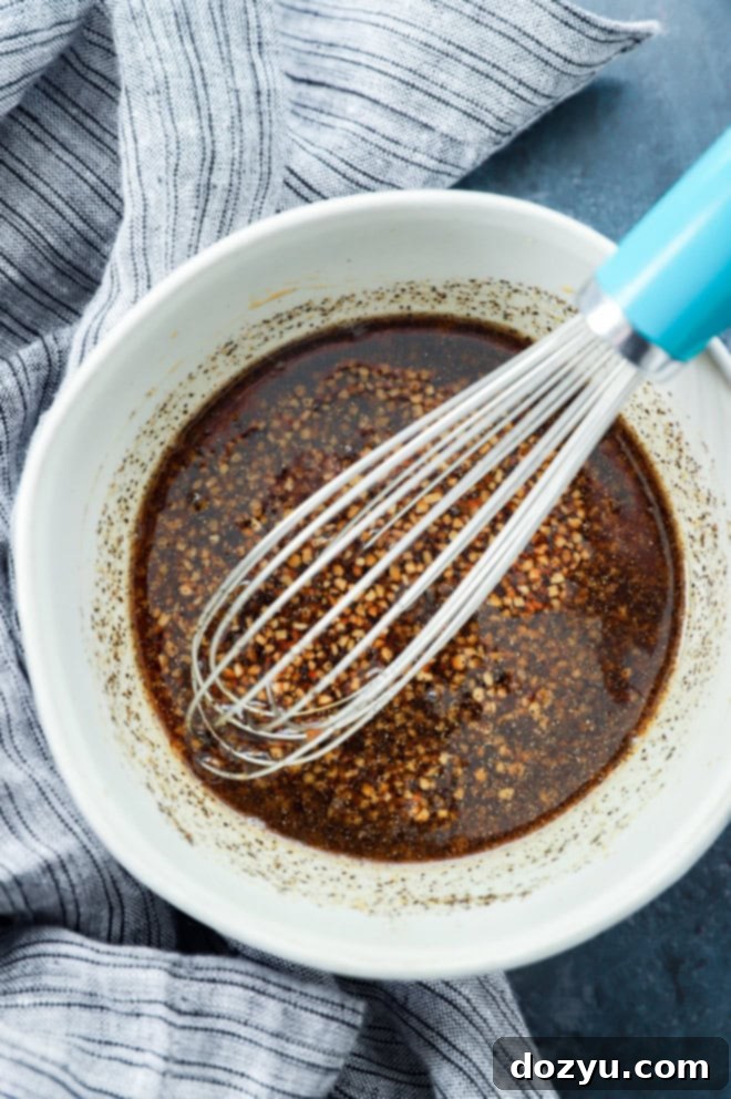 Sweet & Sticky Honey Soy Marinade 4 A bowl of honey soy marinade with a whisk resting inside, alongside a linen towel on a rustic surface.