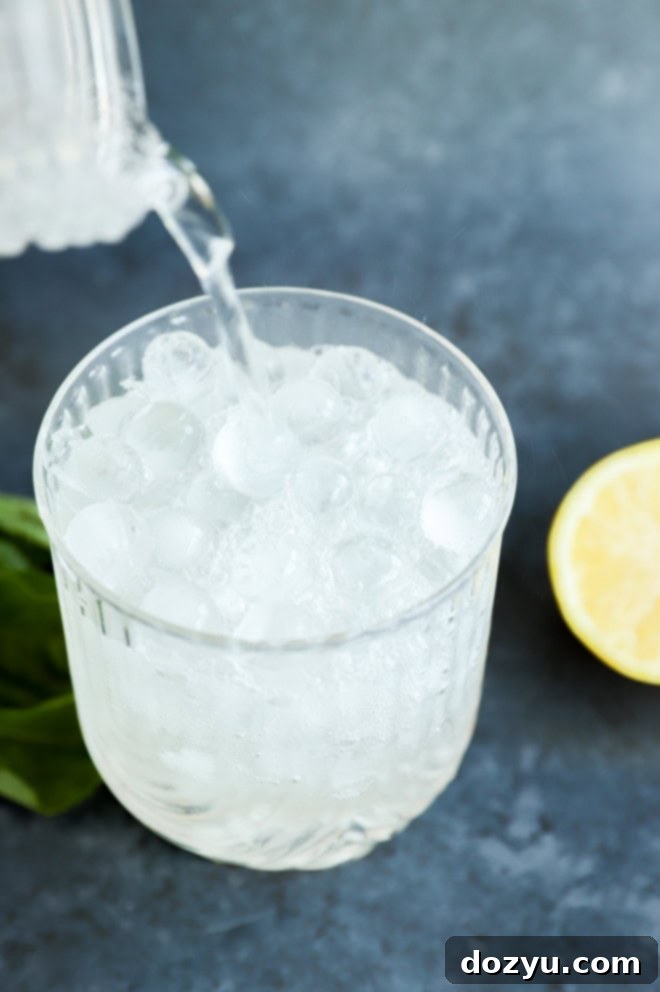 Gin Basil Smash 5 Pouring soda water into a glass with a Gin Basil Smash, enhancing its refreshing quality.