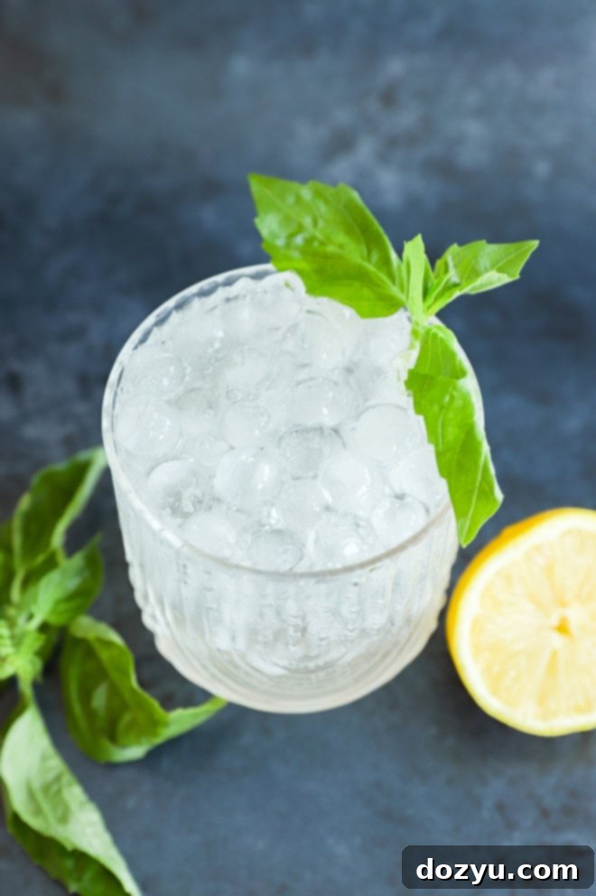 Gin Basil Smash 6 Close-up of a single Gin Basil Smash cocktail garnished with fresh basil and lemon, sitting on a wooden surface.