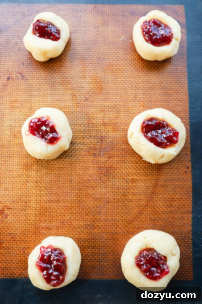 Jammy Raspberry Thumbprints 5 raspberry thumbprint cookies on a baking pan before baking