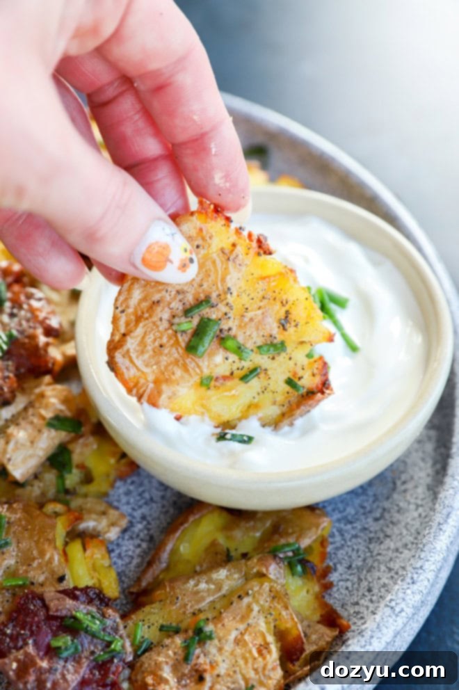 Golden Crispy Smashed Potatoes 8 hand holding a smashed potato dipping into a bowl of sour cream