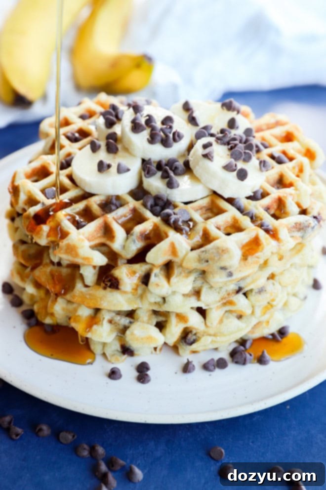 Ultimate Banana Chocolate Chip Waffles 2 Drizzling syrup on a stack of golden banana chocolate chip waffles with fresh fruit and extra chocolate chips