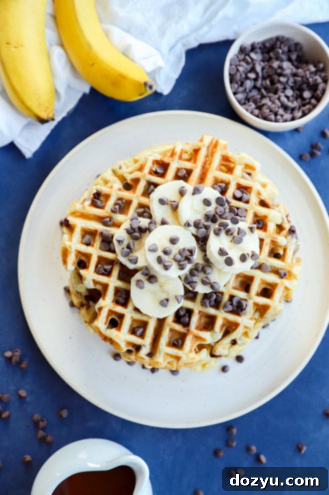 Ultimate Banana Chocolate Chip Waffles 5 Overhead shot of a stack of golden banana waffles on a plate, surrounded by fresh banana slices and a bowl of chocolate chips
