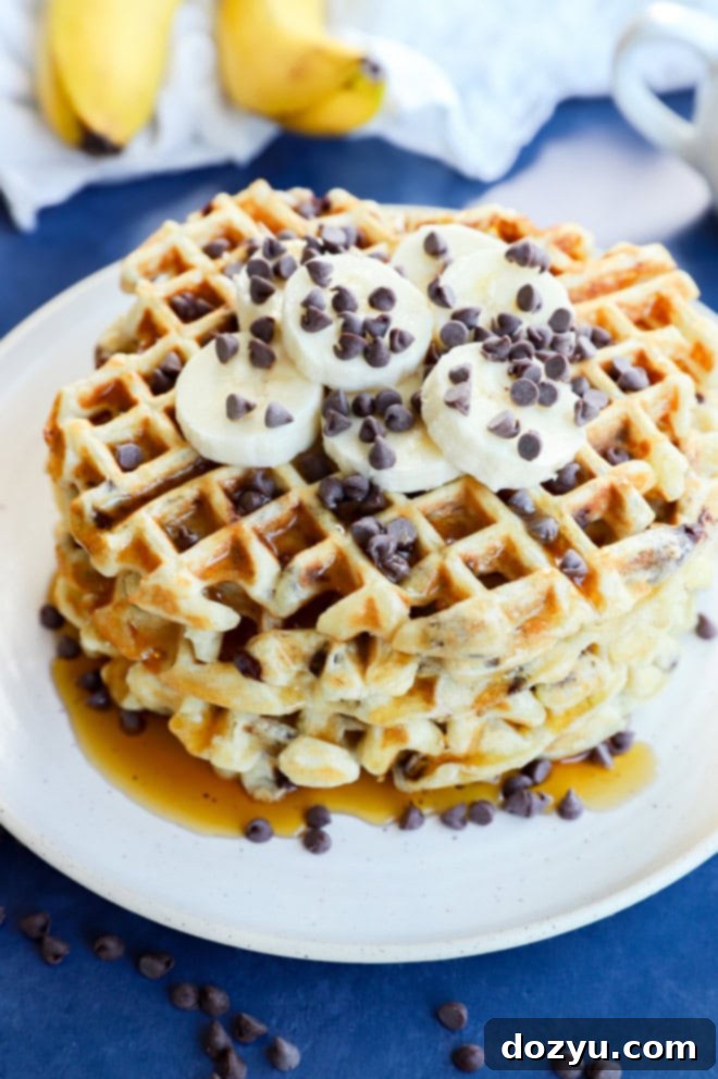 Ultimate Banana Chocolate Chip Waffles 8 Syrup being drizzled over a stack of banana waffles on a plate, with fresh bananas in the background