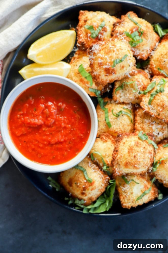 Golden Air Fryer Ravioli 2 air fryer ravioli on plate with lemon slices, marinara sauce, and fresh basil