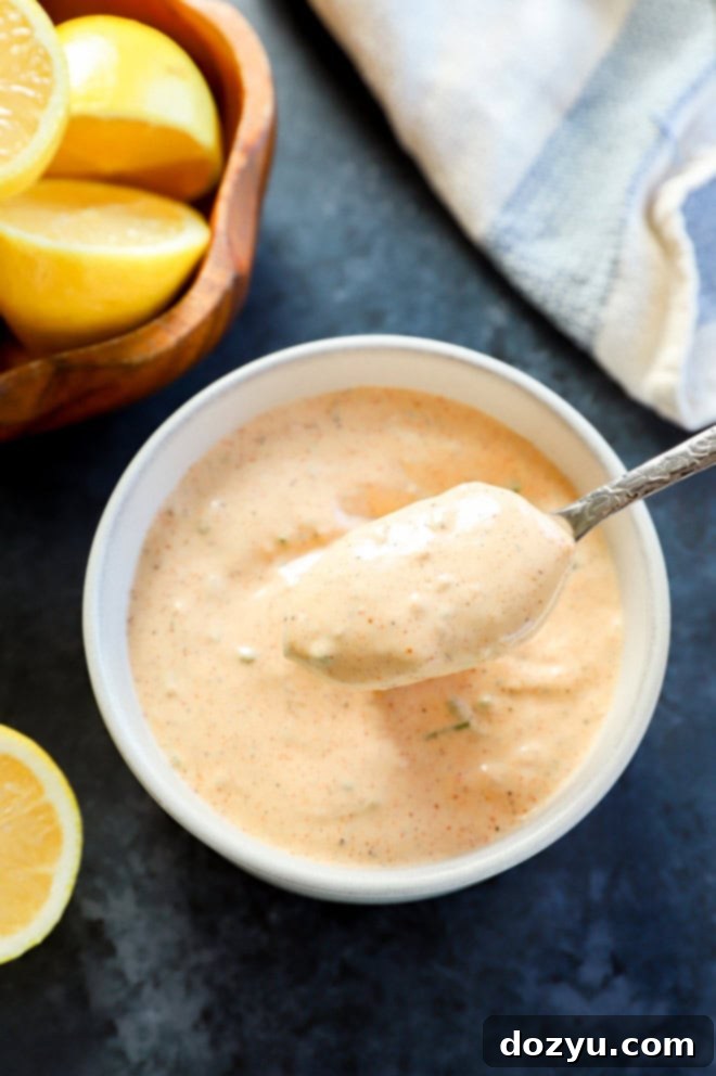 Effortless Crab Cake Sauce 2 spoon lifting out creamy, tangy homemade remoulade sauce for crab cakes from a bowl, with lemon halves in a separate bowl beside it, ready to serve.