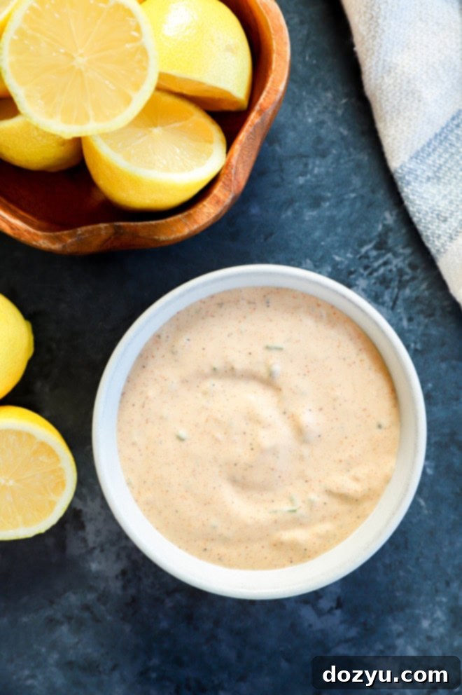 Effortless Crab Cake Sauce 5 Easy homemade remoulade sauce for crab cakes in a serving bowl, garnished with fresh herbs, alongside a bowl of fresh lemons and a blue linen napkin.