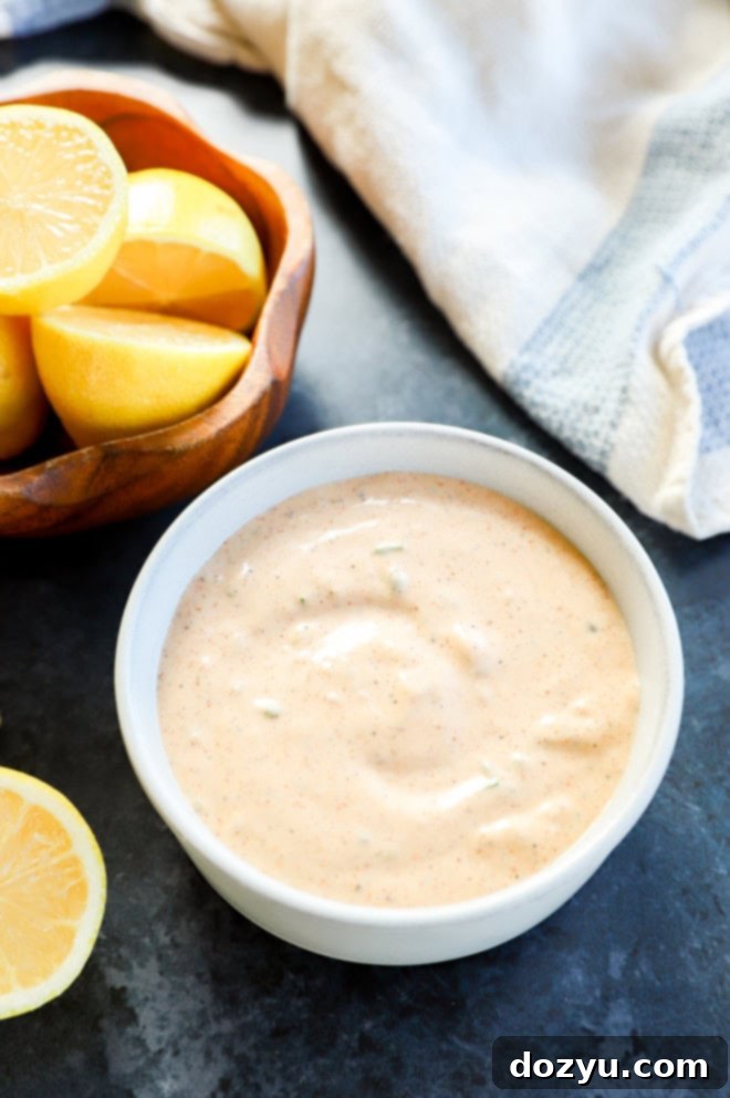 Effortless Crab Cake Sauce 7 creamy seafood sauce for crab cakes in a rustic bowl, garnished with fresh herbs, accompanied by a bowl of lemons and a white linen with blue accents.