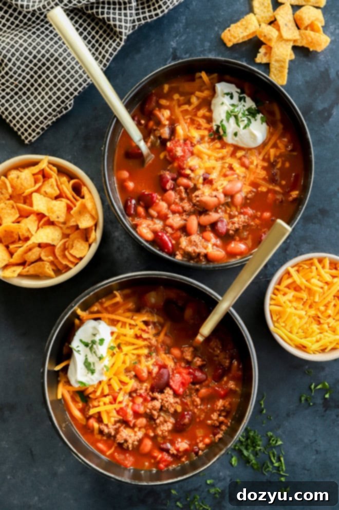 Effortless Instant Pot Chili 2 Two black bowls of homemade Instant Pot Chili with gold spoons, garnished with fresh cilantro and a dollop of sour cream.