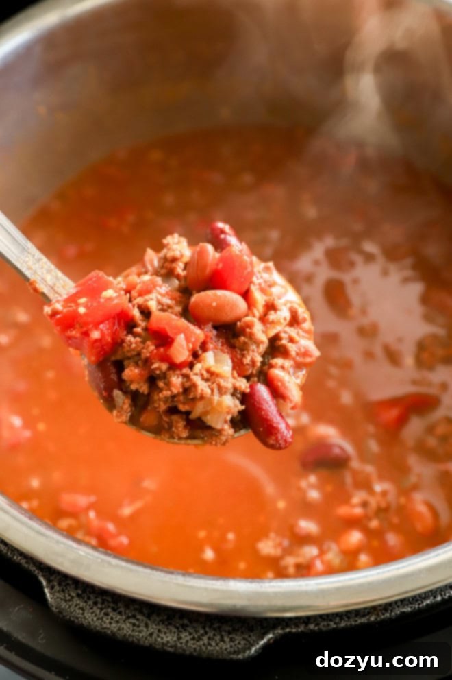 Effortless Instant Pot Chili 4 Ladle scooping out steaming Instant Pot Chili from the Instant Pot insert into a bowl.