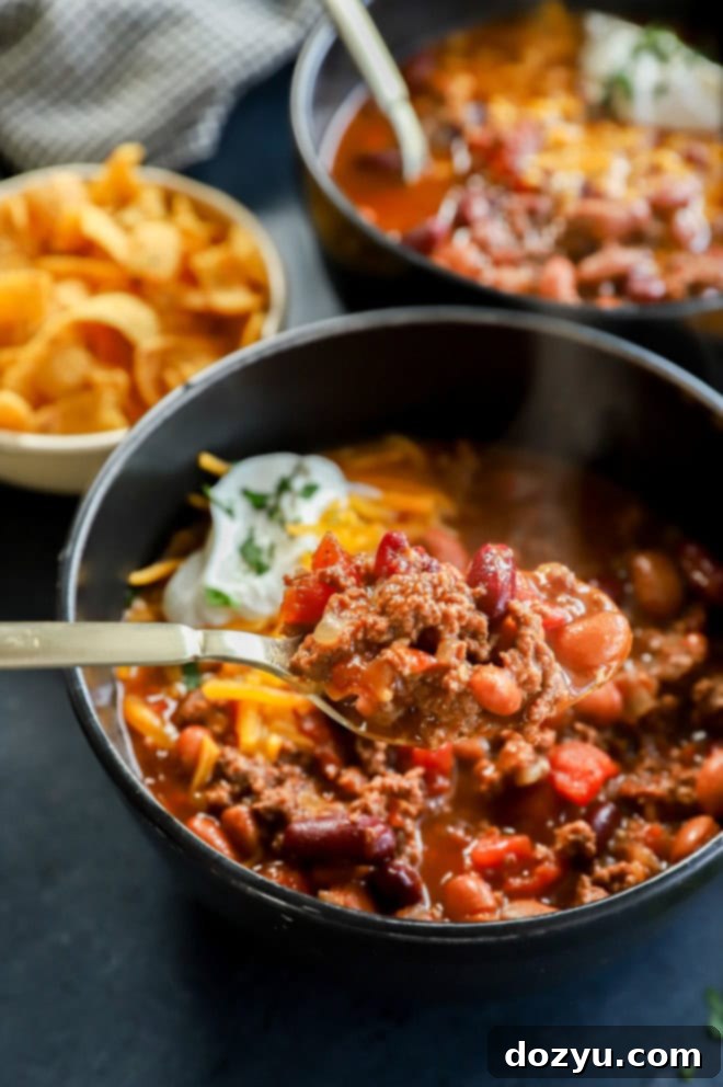 Effortless Instant Pot Chili 6 A bowl of rich beef stew with a gold spoon, adorned with melted cheese and fresh herbs, showcasing the chili's texture.