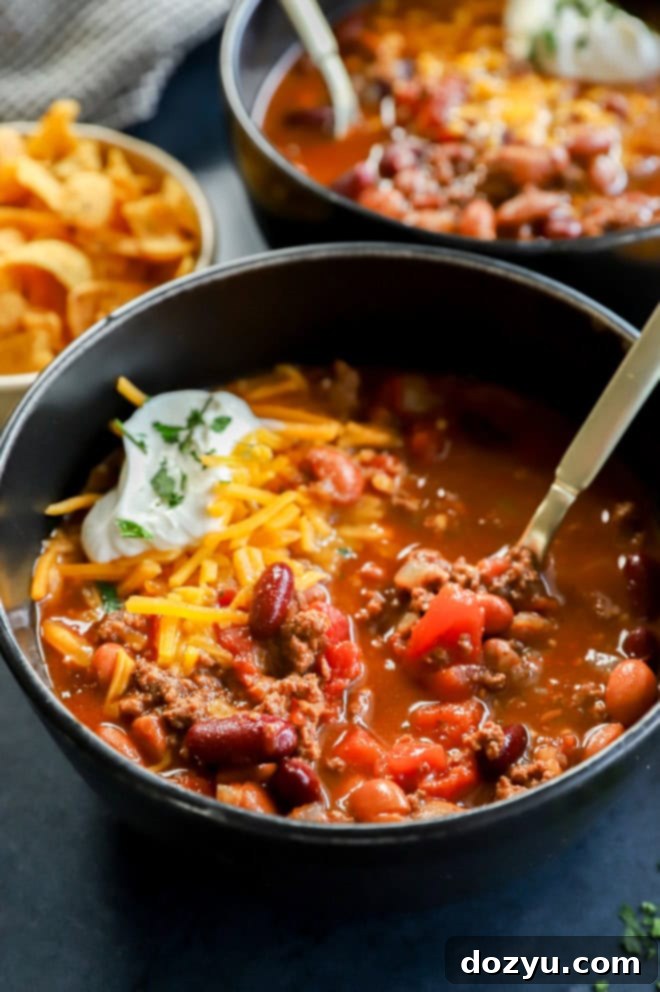 Effortless Instant Pot Chili 7 A bowl of Instant Pot Chili with gold spoon, topped with a generous amount of shredded cheese, sour cream, and fresh herbs.