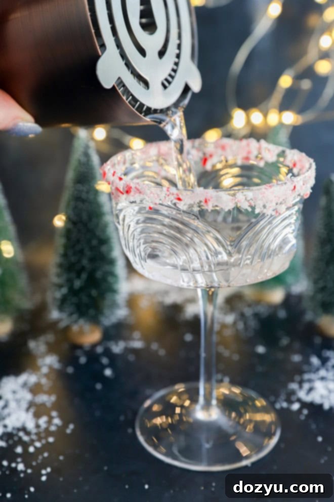 Refreshing Peppermint Martini 4 Close-up of a peppermint martini being poured into a candy cane rimmed coupe glass, showcasing the clear, festive liquid