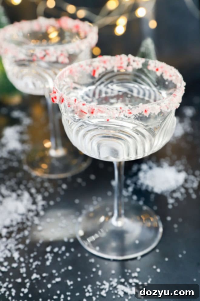 Refreshing Peppermint Martini 7 Beautifully presented peppermint martinis in coupe glasses, adorned with crushed candy cane rims, set against a magical snowy backdrop with fairy lights