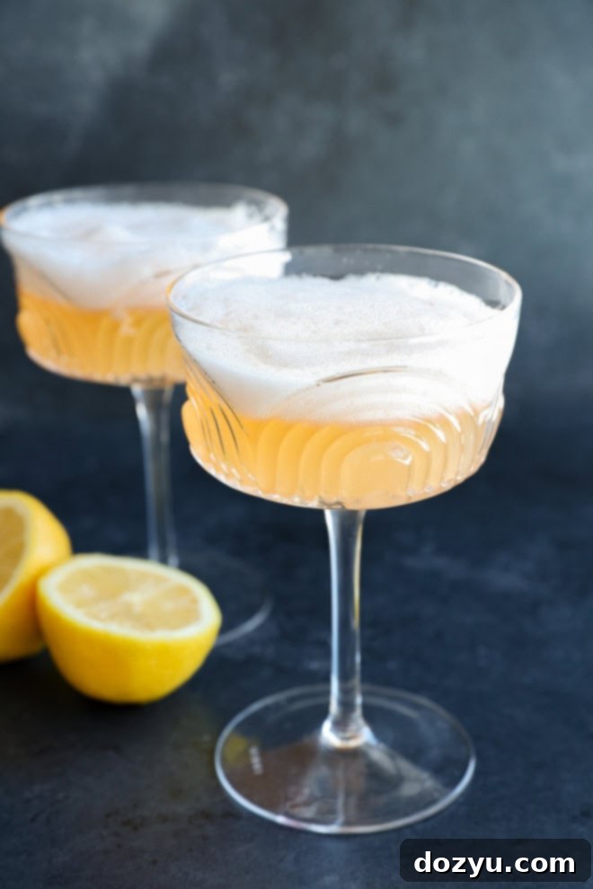 Classic Gin Sour Cocktail 6 Two elegant gin sour cocktails in coupe glasses, adorned with lemon halves