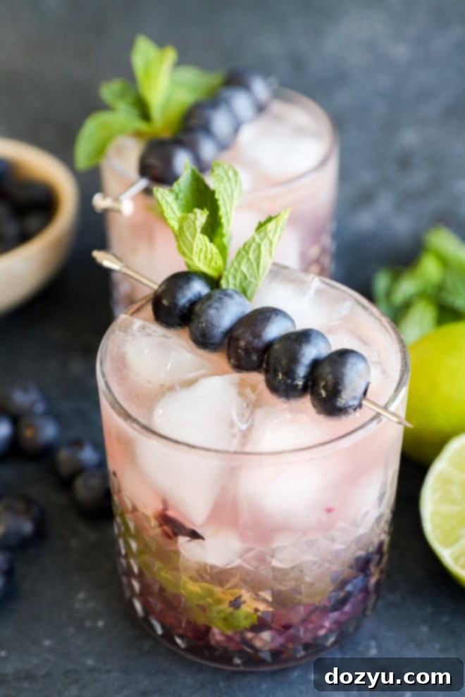 Blueberry Mojito Magic 7 A beautifully presented Blueberry Mojito in a tall glass, garnished with fresh blueberries and mint leaves, ready to be enjoyed.