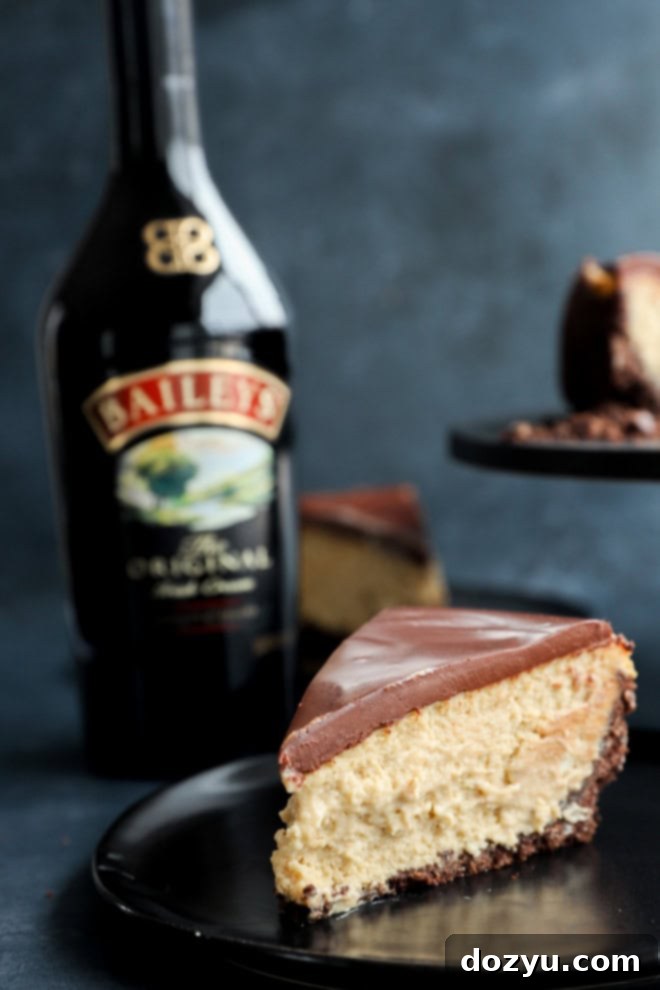 Decadent Baileys Cheesecake 2 A perfectly sliced piece of Baileys cheesecake on a black plate, with a bottle of Irish cream in the soft-focus background, highlighting its rich texture and decadent ganache topping.