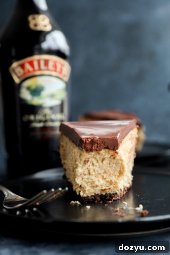 Decadent Baileys Cheesecake 11 A slice of Baileys cheesecake with a bite taken out, resting on a plate, with an out-of-focus bottle of Irish cream in the background.