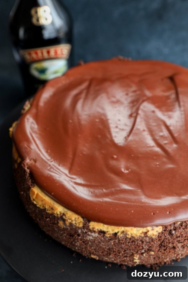 Decadent Baileys Cheesecake 9 A whole Baileys cheesecake displayed on a cake plate, with an Irish cream bottle in the background, ready to be served.