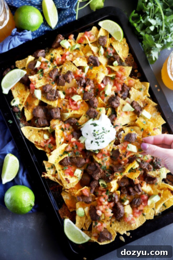 Close-up of perfectly layered Carne Asada Nachos, showcasing the depth of ingredients.