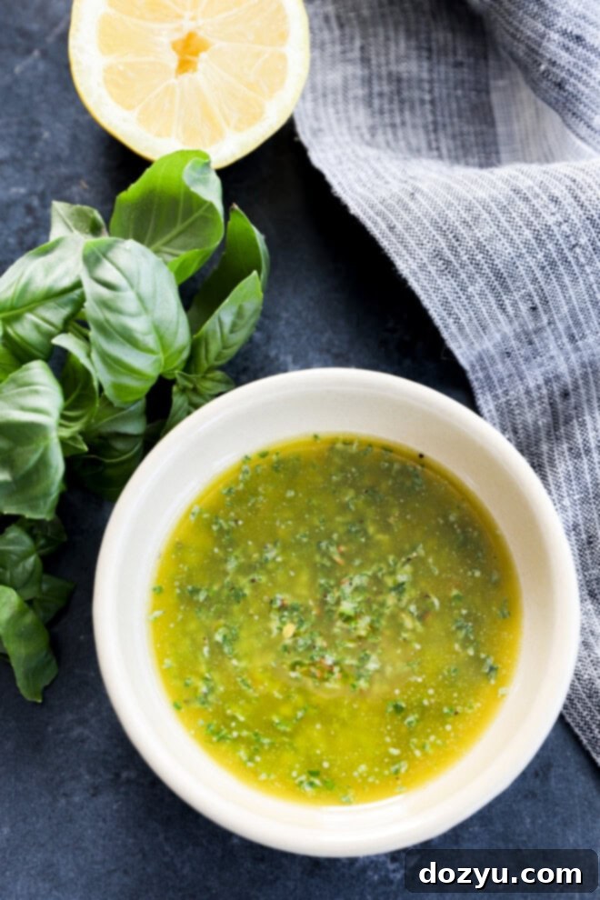 The Magic of Basil Oil 2 A bowl of vibrant green basil oil, garnished with fresh basil sprigs and half a lemon, set on a stylish grey linen background.