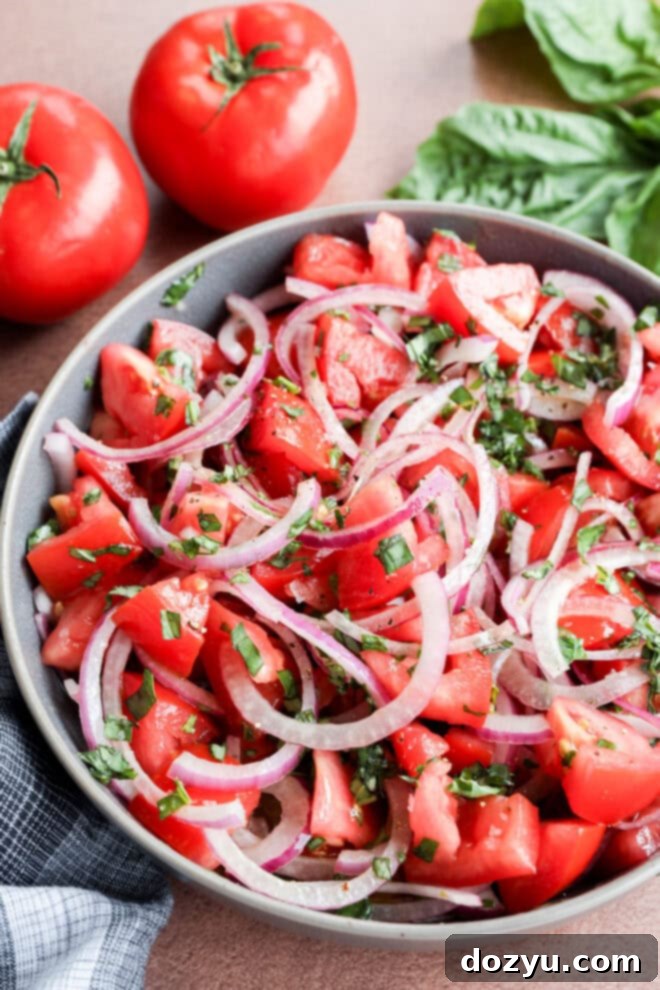 Zesty Tomato Onion Salad 7 Tomato onion salad in a bowl with tomatoes and fresh basil behind it