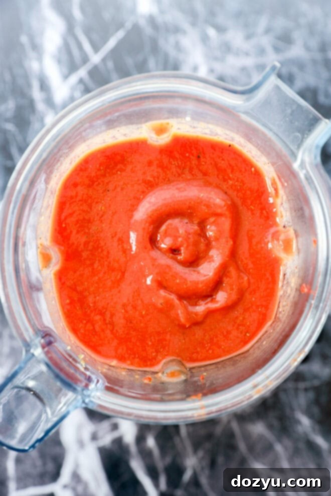Ultimate Pizza Sauce 5 A blender filled with bright red Best Pizza Sauce, viewed from above, sits on a gray and white marble countertop.