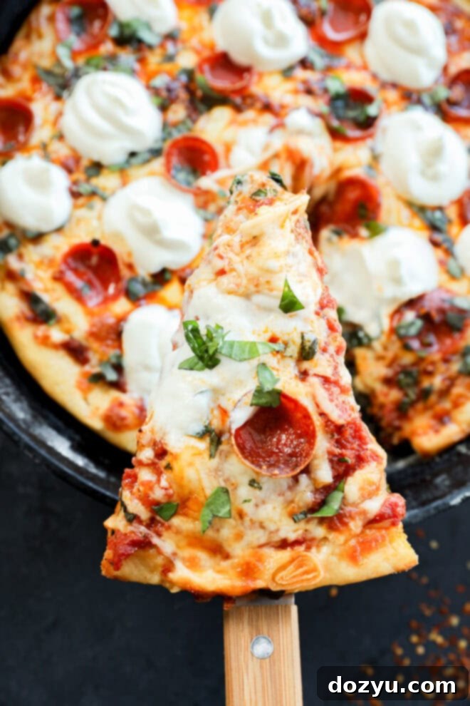 Sizzling Skillet Pepperoni Pie 9 A close-up of a spicy pizza with pepperoni, melted mozzarella, fresh basil, and tomato sauce. A single slice is being lifted from the whole pizza with a wooden spatula.