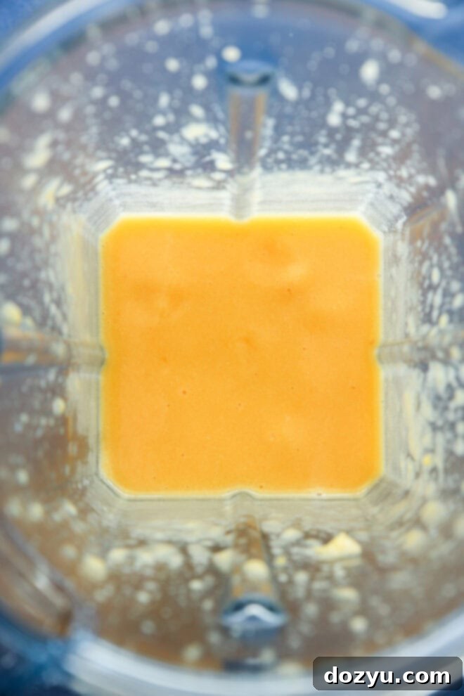 A top-down view of a blender containing a smooth, vibrant orange peach puree, with some subtle splatters of the mixture on the sides of the blender jar, ready for cocktail preparation.