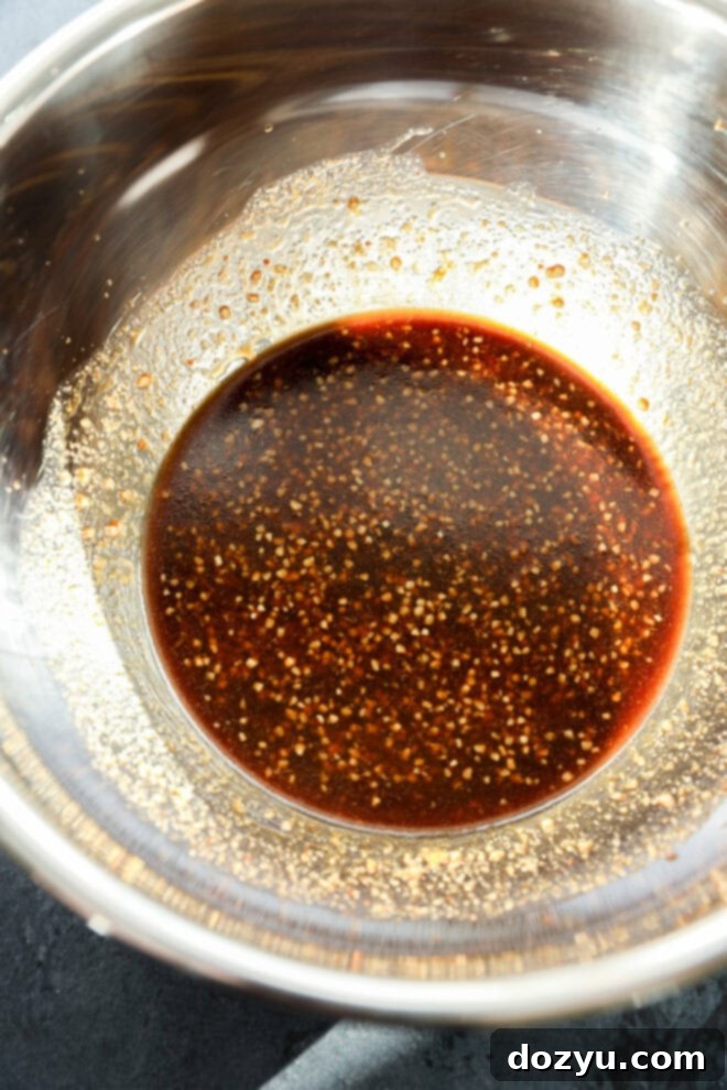 Savory Asian Chicken Marinade 4 A metal mixing bowl containing a dark, slightly thick Asian Chicken Marinade with visible flecks of seasoning and spices.