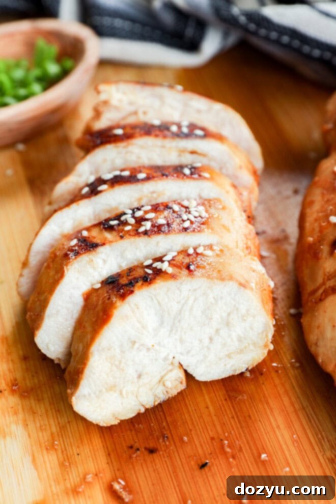Savory Asian Chicken Marinade 8 Sliced cooked chicken breast, marinated in a savory Asian Chicken Marinade and sprinkled with sesame seeds, is arranged neatly on a wooden cutting board with a small bowl of chopped green onions in the background.