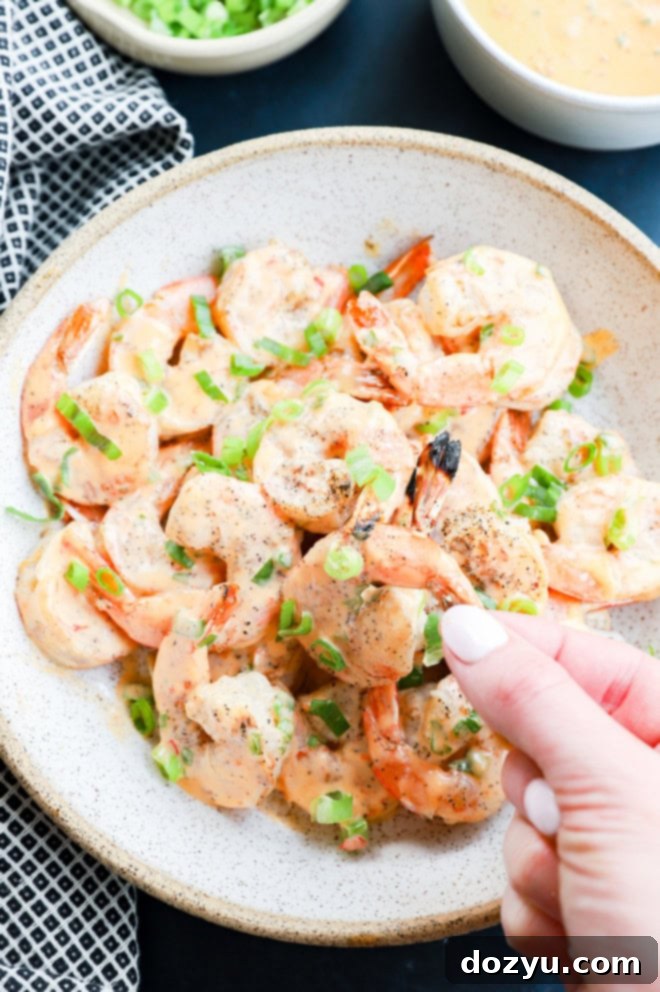Sizzling Bang Bang Prawns 11 A hand holding a grilled bang bang shrimp over a bowl of sauced shrimp.