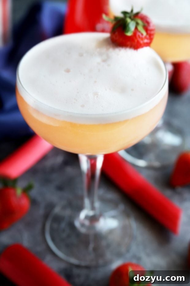 A beautifully layered Strawberry Rhubarb Gin Fizz cocktail, showcasing its refreshing pink hue and frothy top.