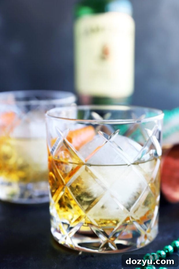 The Jameson Old Fashioned 2 Side photo image of an old fashioned cocktail, showcasing a single drink in a rocks glass with a large ice sphere and orange peel garnish