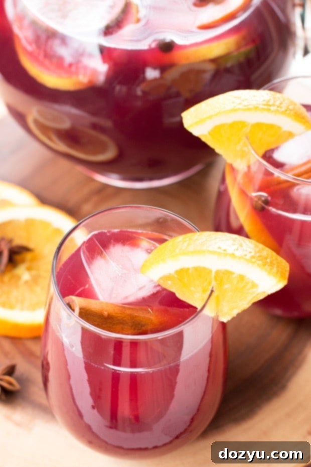Big Batch Holiday Sangria in a glass pitcher with fruit slices and ice