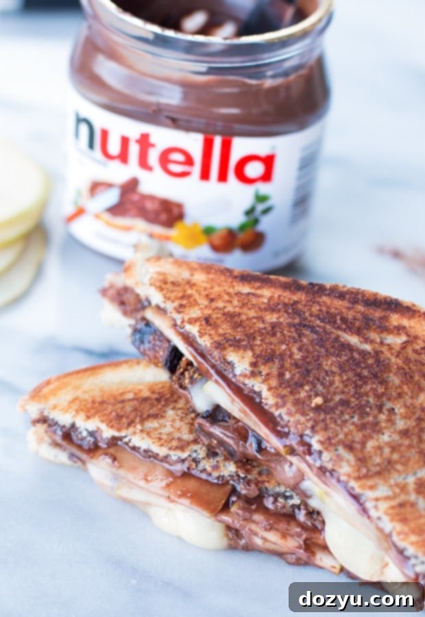 Melted chocolate and creamy brie oozing from a perfectly golden brown Grilled Nutella, Brie, Pear & Fig Sandwich, served on a rustic cutting board.