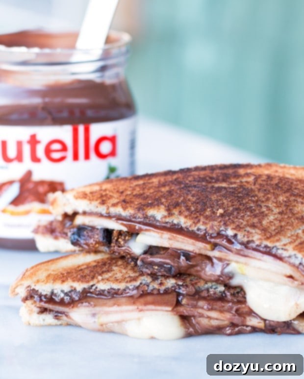 A cross-section of a warm and inviting Grilled Nutella, Brie, Pear & Fig Sandwich, revealing its perfectly melted layers of chocolate, cheese, and fruit.