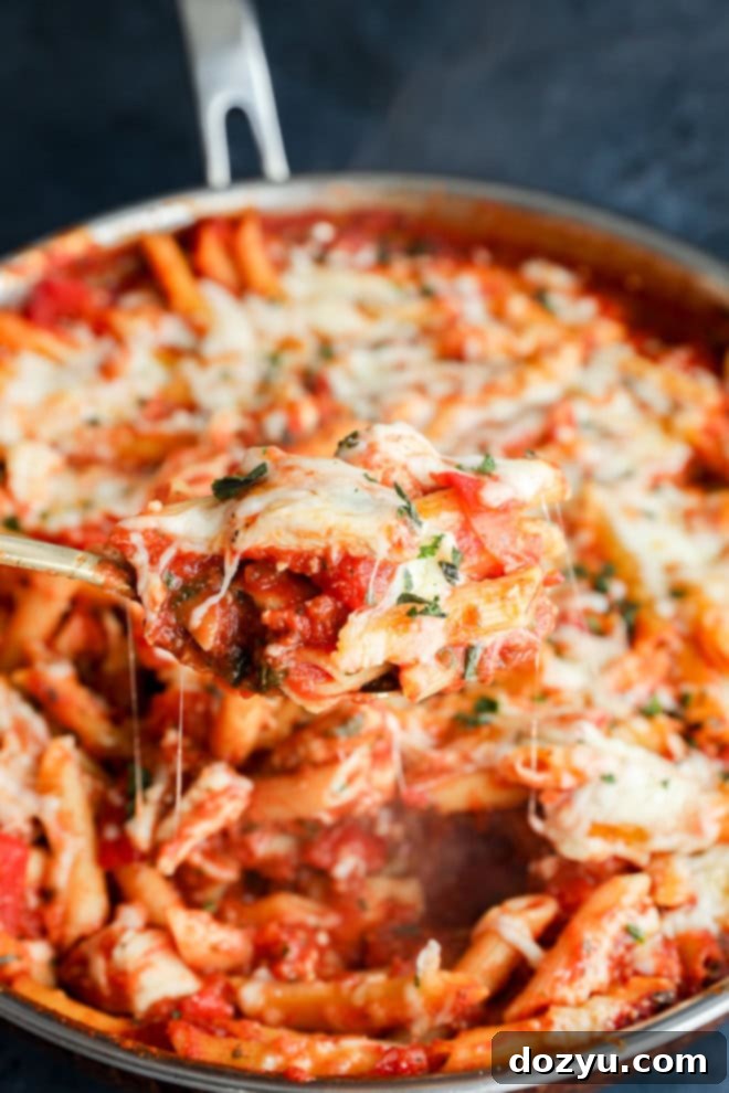 spoon lifting out gooey chicken parmesan pasta from the skillet