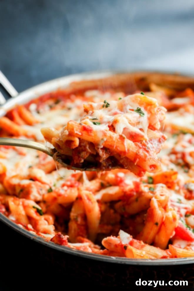 spoon lifting out italian penne dish with poultry and marinara sauce and cheese