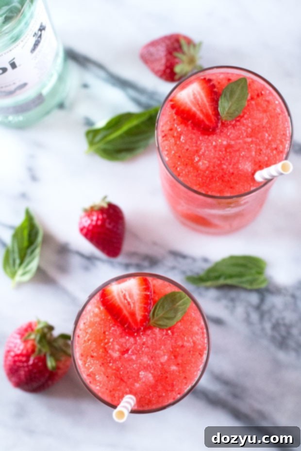 Delicious Strawberry Basil Frozen Daiquiri cocktail in a tall glass, garnished with fresh basil and a strawberry slice