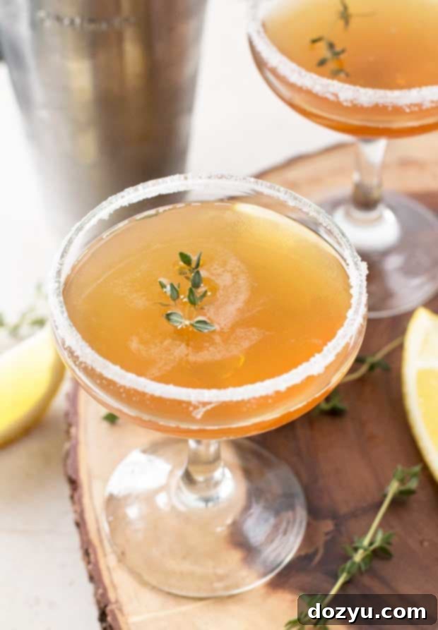 Lemon Thyme Sidecar cocktail in a sugar-rimmed glass with a sprig of thyme