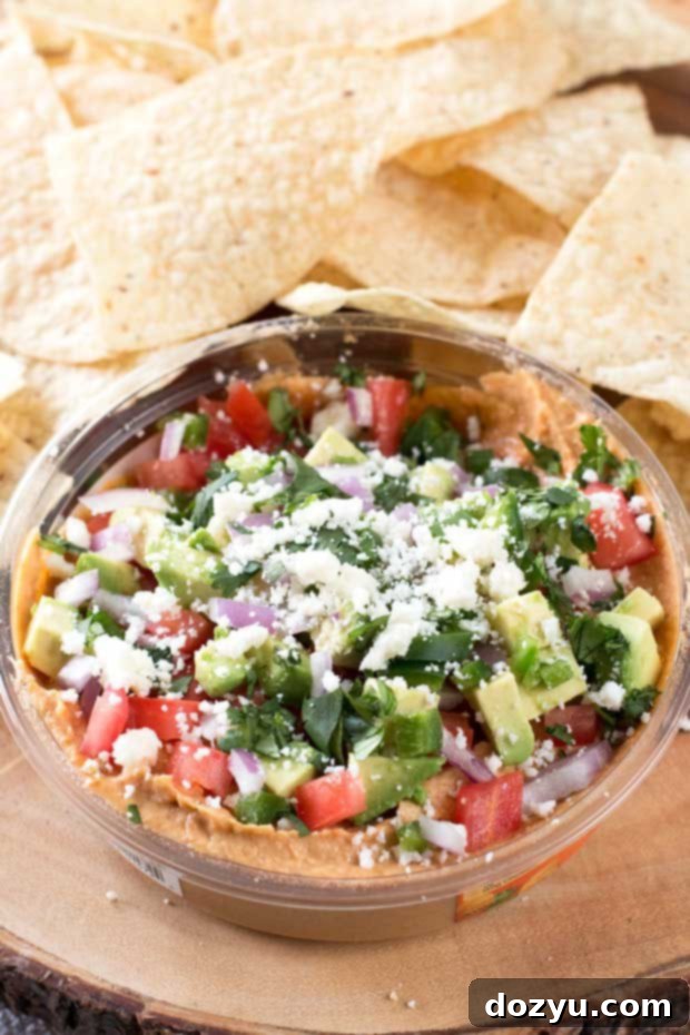 Close-up of a serving spoon scooping into the layered South of the Border Hummus, showcasing its fresh toppings.